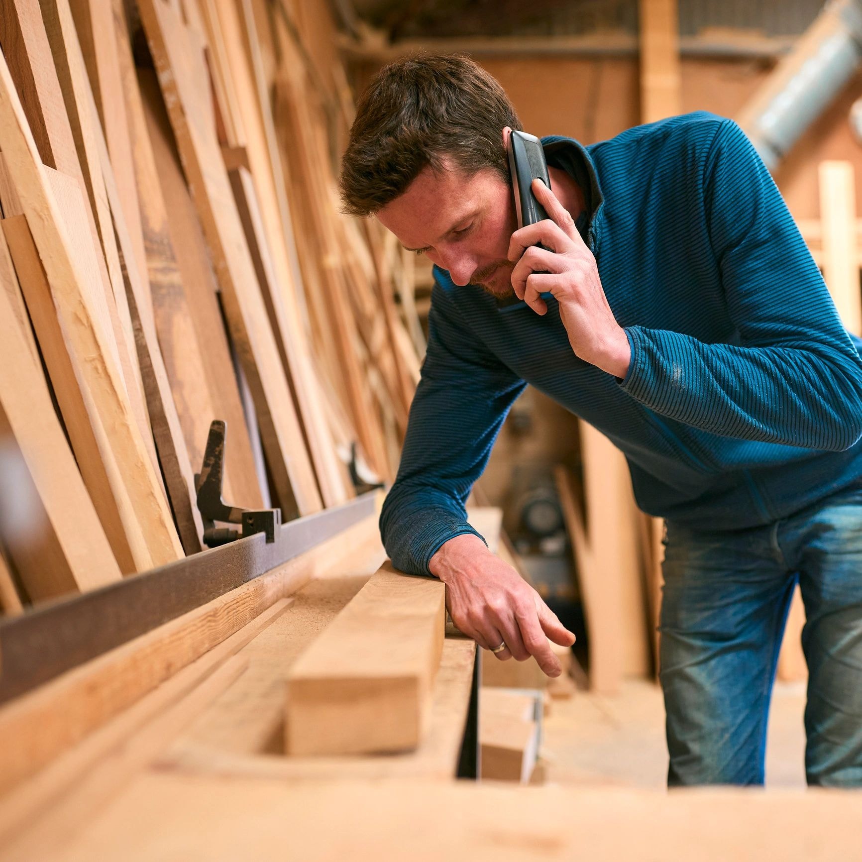 A craftsperson at a woodworking bench, speaking on the phone